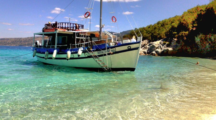 Tour boat anchored at the South Lagoon Sandbank in Corfu with crystal-clear shallow waters and passengers swimming during a half-day boat excursion.
