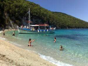 Tour boat anchored at the South Lagoon Sandbank in Corfu with crystal-clear shallow waters and passengers swimming during a half-day boat excursion.