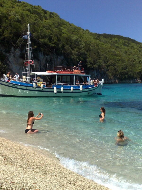 Tour boat anchored at the South Lagoon Sandbank in Corfu with crystal-clear shallow waters and passengers swimming during a half-day boat excursion.