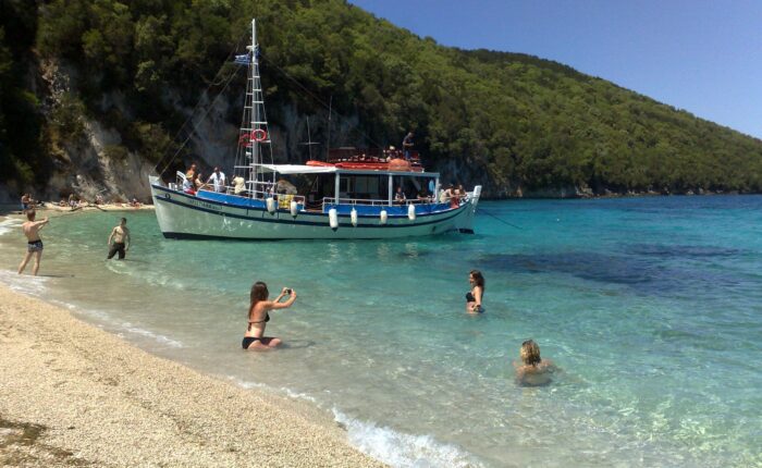 Tour boat anchored at the South Lagoon Sandbank in Corfu with crystal-clear shallow waters and passengers swimming during a half-day boat excursion.