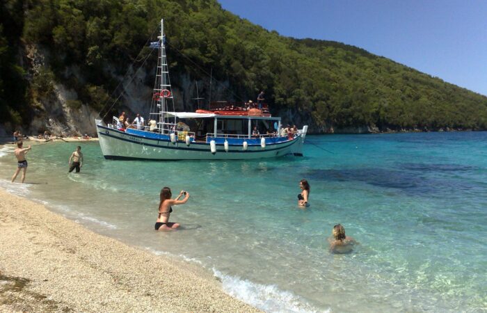 Tour boat anchored at the South Lagoon Sandbank in Corfu with crystal-clear shallow waters and passengers swimming during a half-day boat excursion.