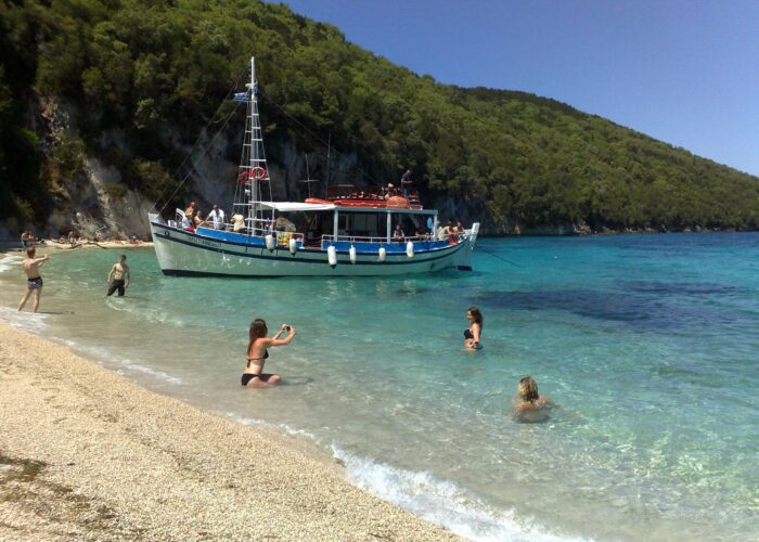 Tour boat anchored at the South Lagoon Sandbank in Corfu with crystal-clear shallow waters and passengers swimming during a half-day boat excursion.