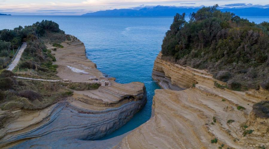 Paleokastritsa beach in Corfu with crystal-clear turquoise waters, surrounded by lush green hills and dramatic cliffs.